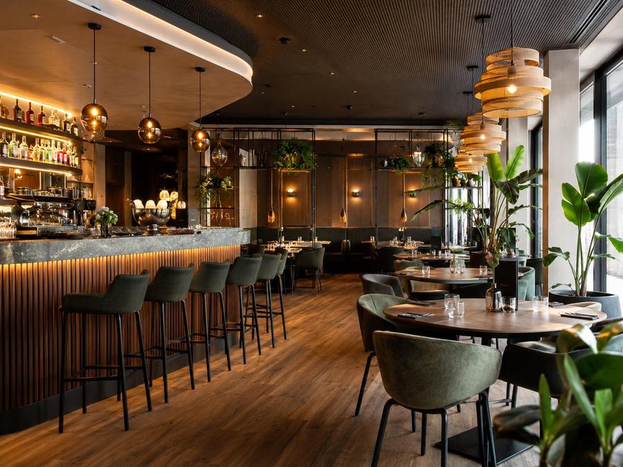 Restaurant-Innenraum mit Bar, Designerleuchten, dunklem Holz und grünen Stühlen